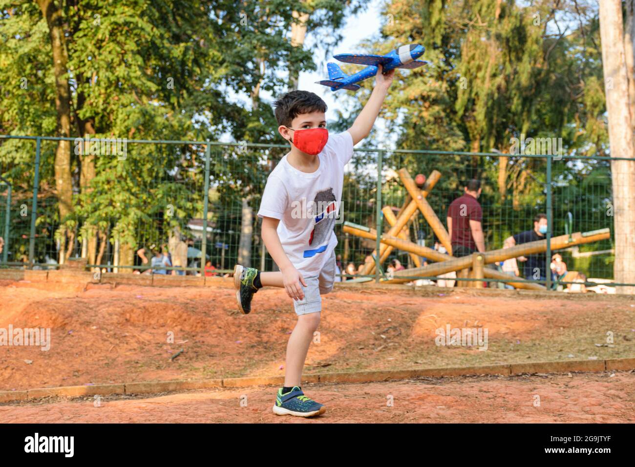 Das 8-jährige Kind balanciert auf einem Fuß und hält sein blaues Styroporflugzeug auf einem öffentlichen Platz. Stockfoto