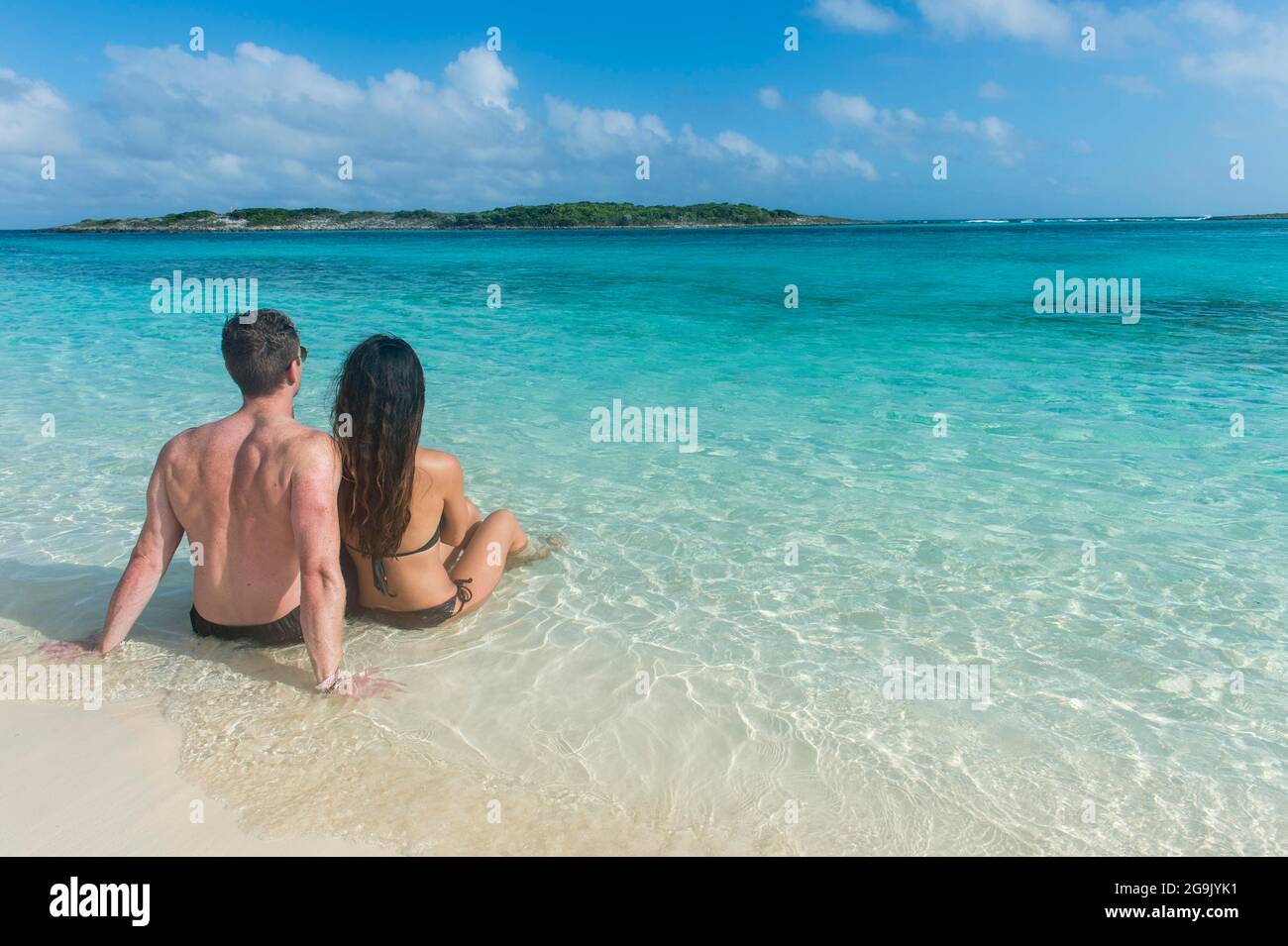 Pärchen, die an einem weißen Sandstrand im türkisfarbenen Wasser der Exumas, Bahamas, Karibik, sitzen Stockfoto