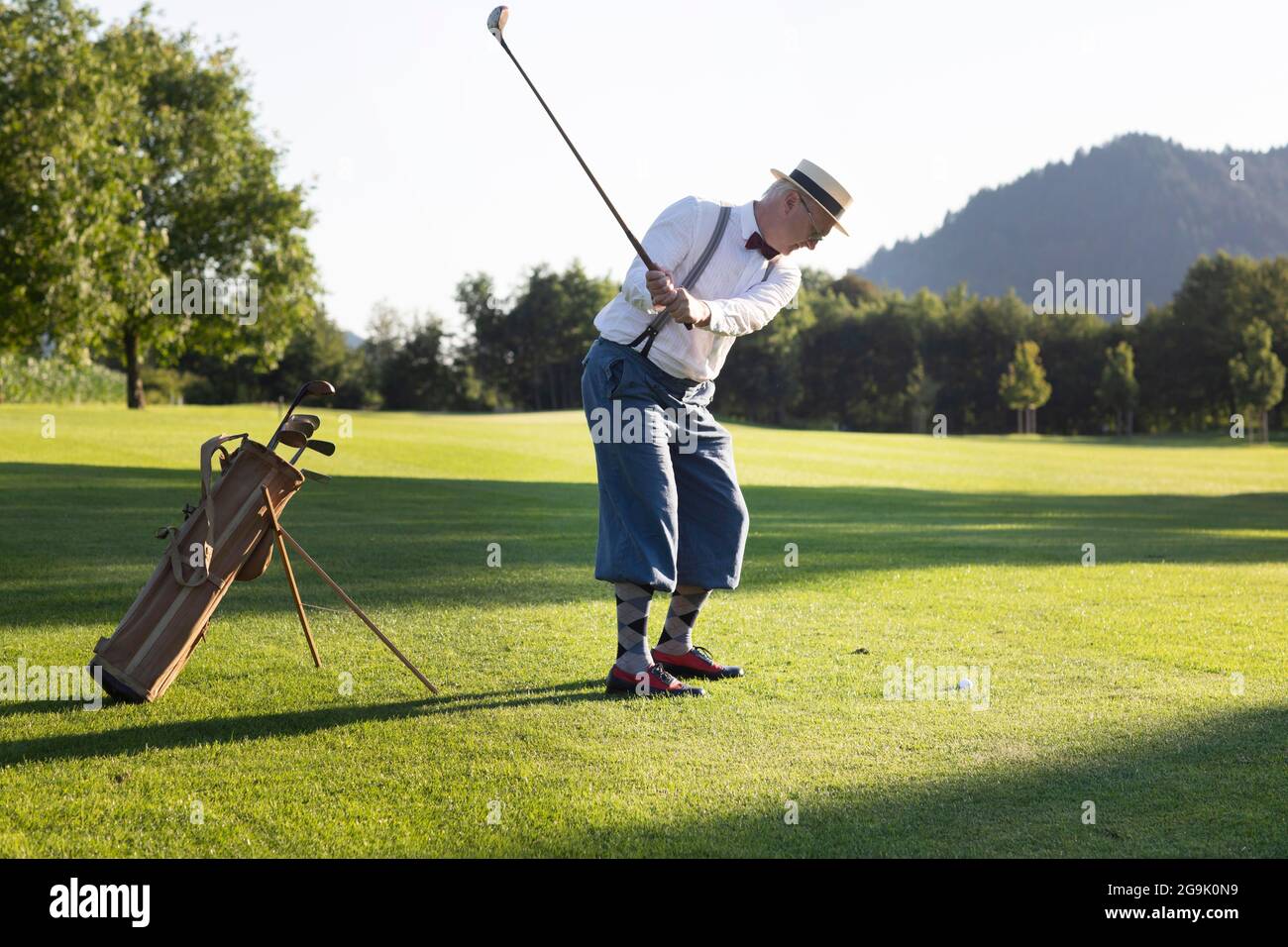 Ein älterer Mann mit Strohhut und Knickerbockern, die auf einem Golfplatz Hickory Golf spielen Stockfoto