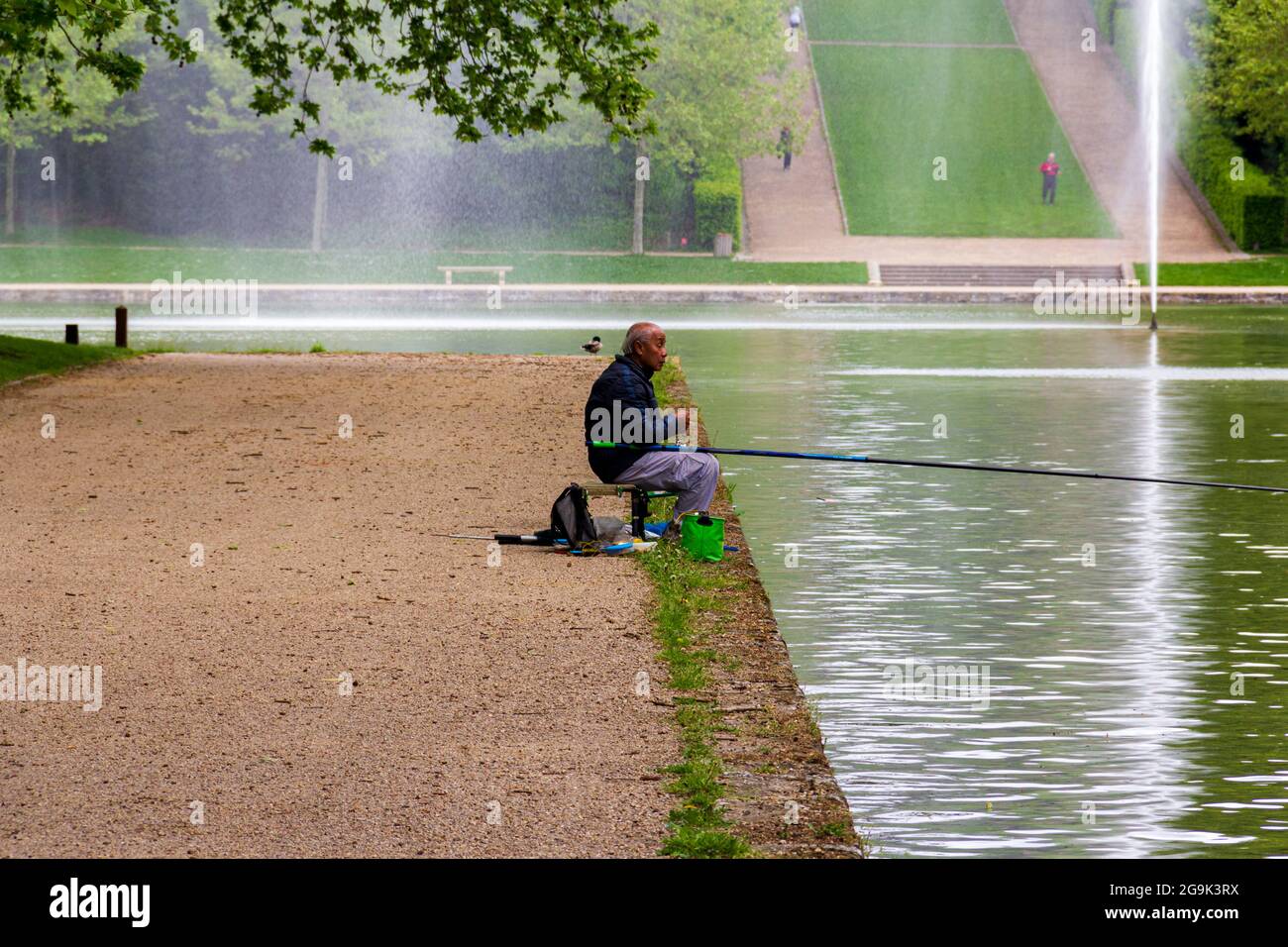 Älterer brauner Mann, der in einem See mit formellen Gärten in Sceaux, Frankreich, fischt Stockfoto