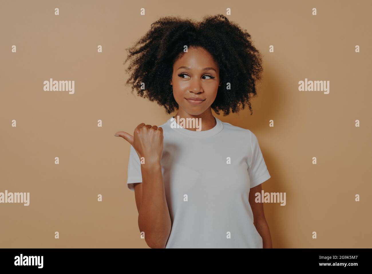 Ziemlich lockig behaarte afrikanische Frau zeigt Daumen beiseite, empfiehlt promo und wirbt Produkt Stockfoto