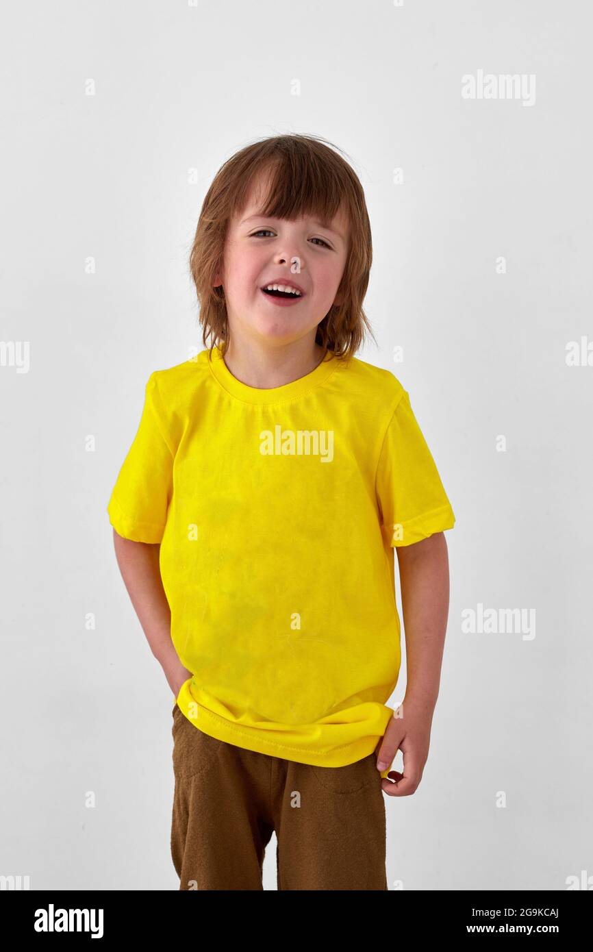 Froher Junge im gelben T-Shirt, der vor weißem Hintergrund steht und wegschaut Stockfoto