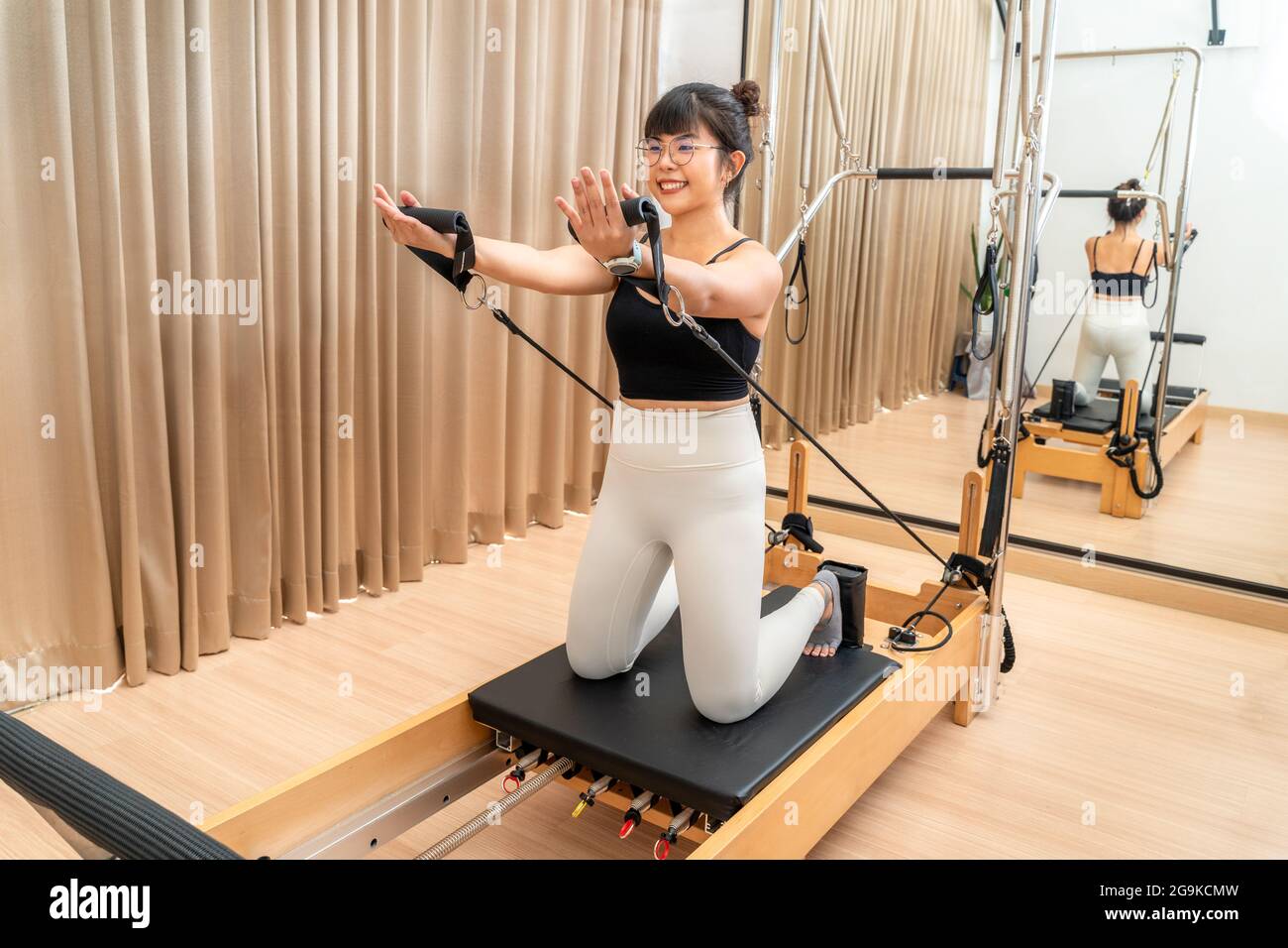 Junge asiatische Frau arbeiten auf Pilates Reformer Maschine während sie Training für Gesundheitsübungen Stockfoto