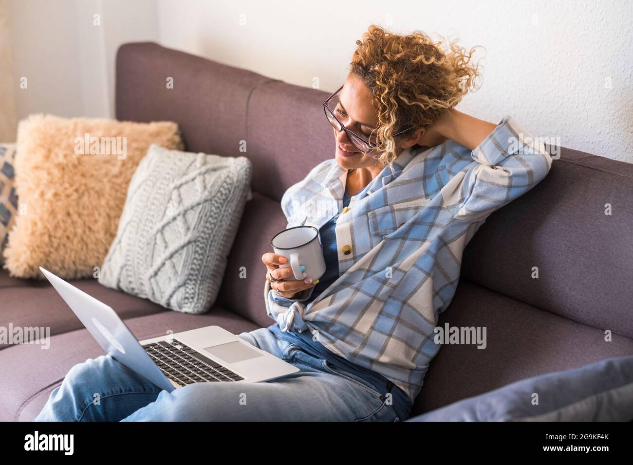 Erwachsene Frau haben nach der Arbeit mit Laptop-Computer im Sofa Home Office entspannen - moderne Arbeit smart arbeiten Menschen Lebensstil - weiblich genießen Videoanruf und c Stockfoto