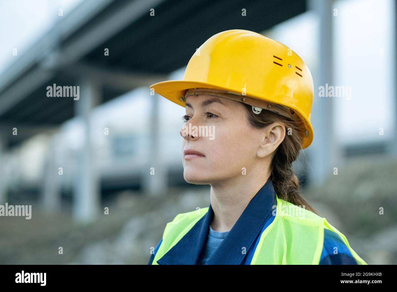 Nahaufnahme einer jungen Frau im Arbeitshelm, die wegschaut, während sie auf der Baustelle im Freien steht Stockfoto