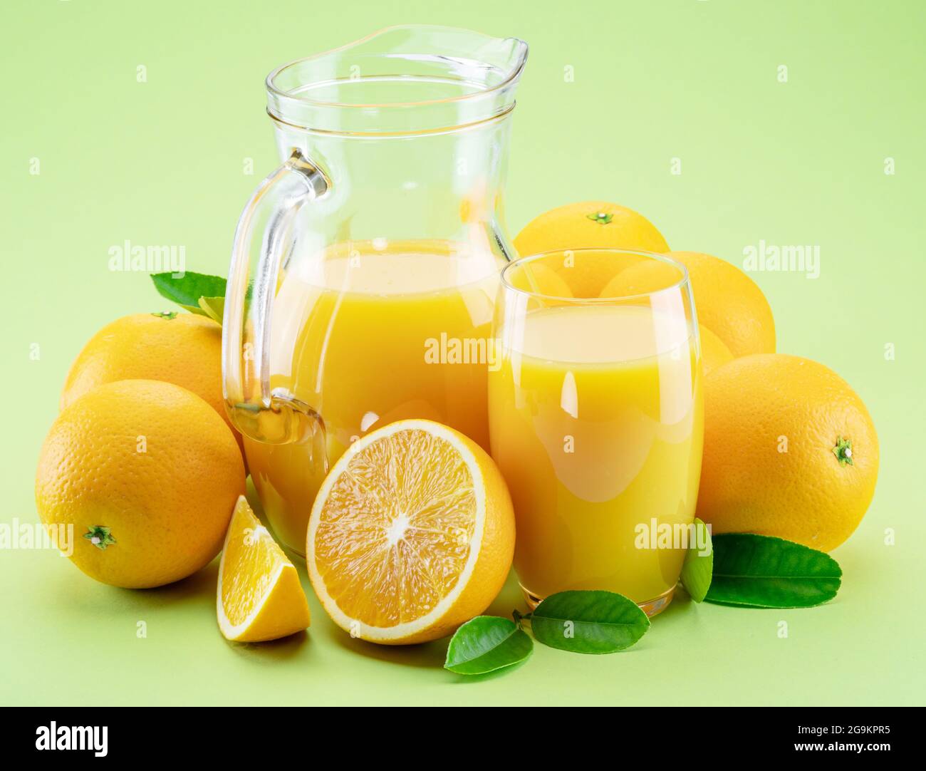 Gelb-orange Früchte und frischer Orangensaft isoliert auf hellgrünem Hintergrund. Stockfoto