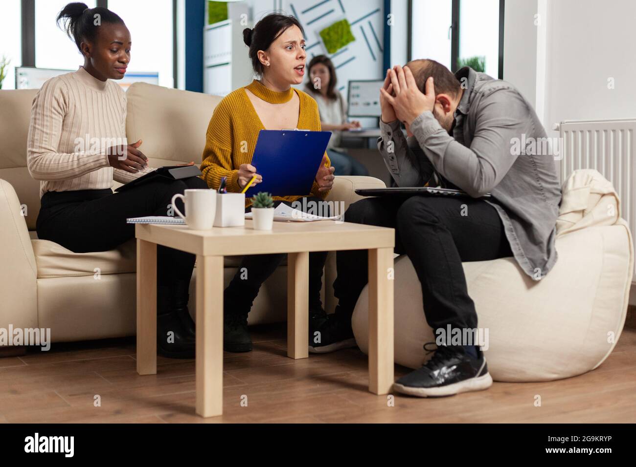 Verärgerte Managerin, die sich über einen schlechten Geschäftsvertrag widersetzt, verschiedene Kollegen, die sich über ein Dokument streiten, das auf der Couch am Schreibtisch sitzt, Partner, die sich widersetzen. Stockfoto