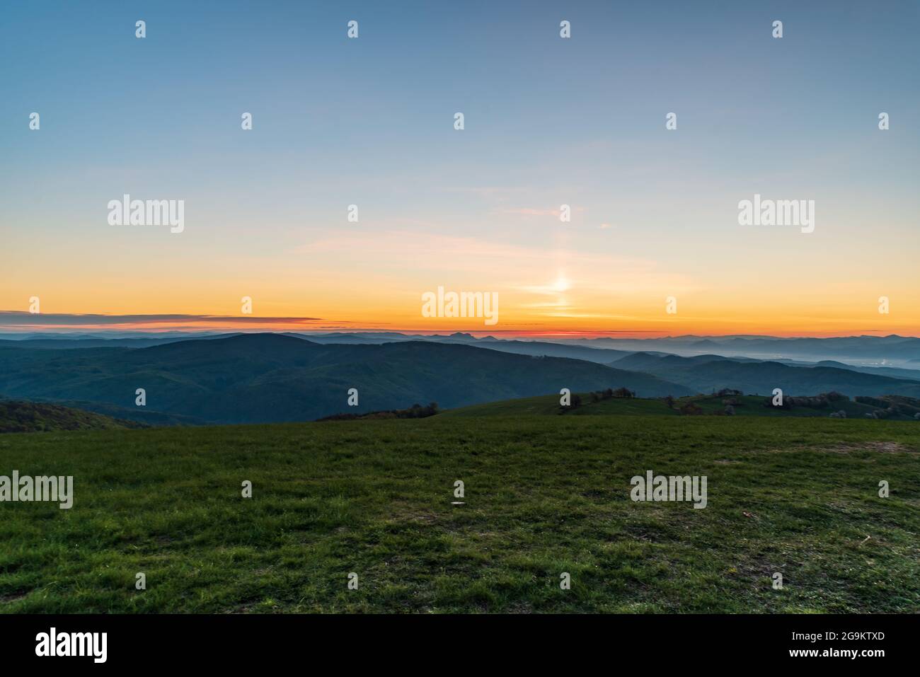 Blick am frühen Morgen vom Machnac-Hügel in Biele Karpaty Berge in der Slowakei mit Wiese, vielen Hügeln und orangefarbenem Himmel Stockfoto