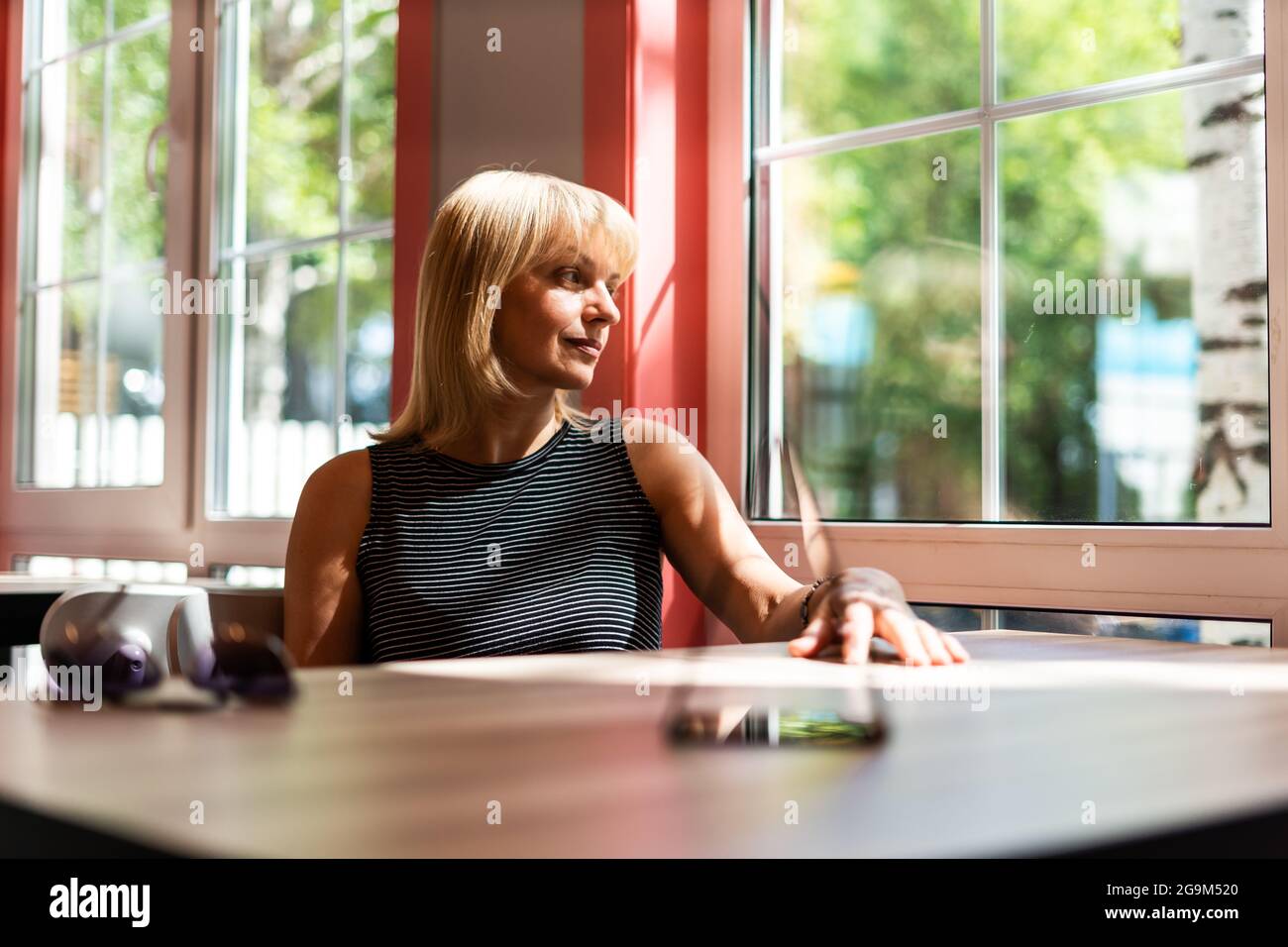 Nachdenkliche Erwachsene reife Frau, die durch das Fenster schaut, während sie am Tisch im Café sitzt. Frau mittleren Alters entspannend. Stockfoto