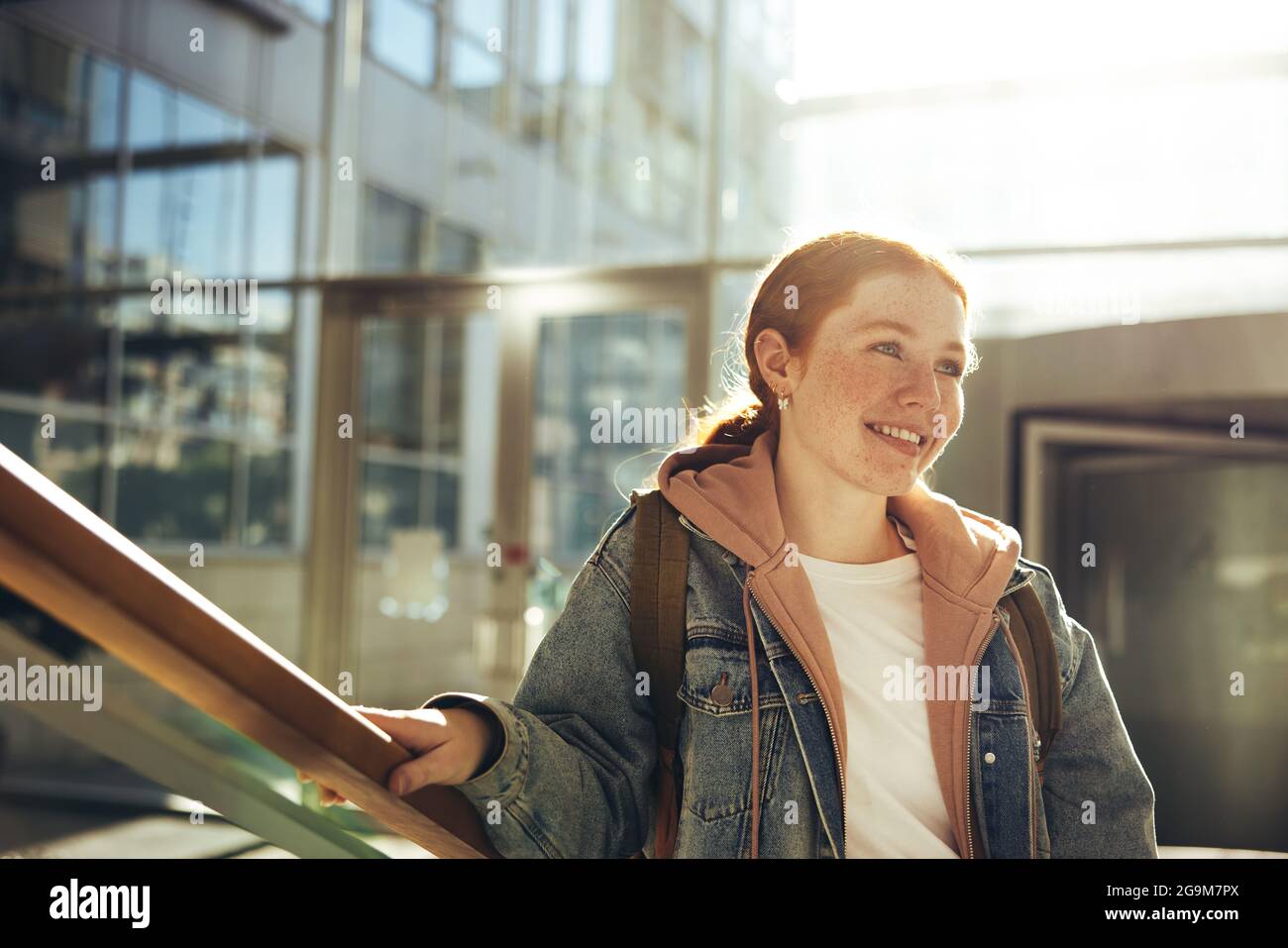 Junge Frau schaut weg, während sie auf dem College-Campus steht. Frau an der Universität für Gelegenheitsklässler. Stockfoto