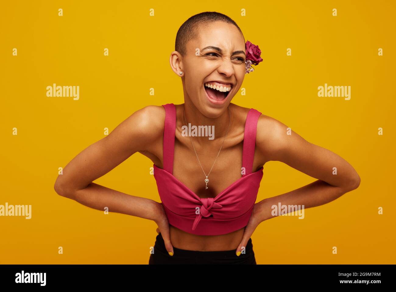 Frau in stilvollem Outfit auf gelbem Hintergrund. Model steht mit den Händen auf der Hüfte und schaut weg und lacht. Stockfoto