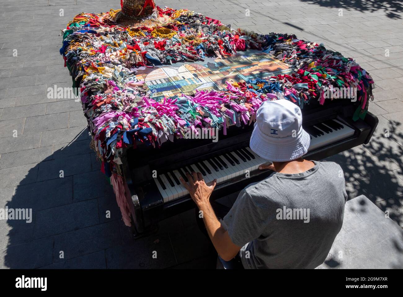 Ein israelischer Mann spielt auf dem Zion-Platz in Jerusalem in Israel Klavier, umhüllt von bunten Kunstfaserstreifen Stockfoto