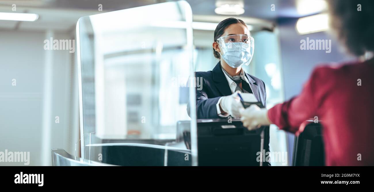 Flugbegleiter mit Schutzmaske und Gesichtsschutz, der den Passagier am Flughafen unterstützt. Der Mitarbeiter am Check-in-Schalter übergibt der Reise eine Bordkarte Stockfoto