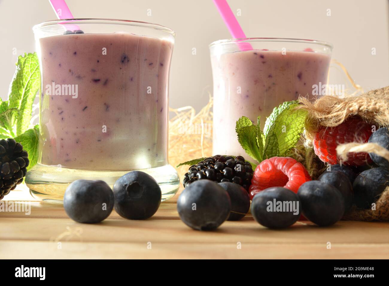 Waldbeerjoghurt Smoothie in Gläsern auf Holztisch mit Sack voller Heidelbeeren, Brombeeren Himbeeren weißen isolierten Hintergrund Stockfoto