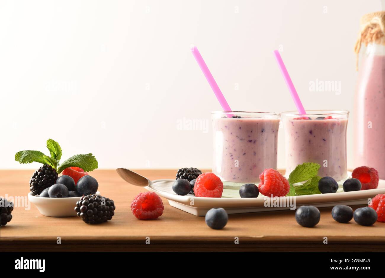 Waldfrucht-Smoothie mit Milch in Glasgläsern und auf weißem Teller und Früchten auf einem Holztisch und weißem isolierten Hintergrund. Vorderansicht. Stockfoto
