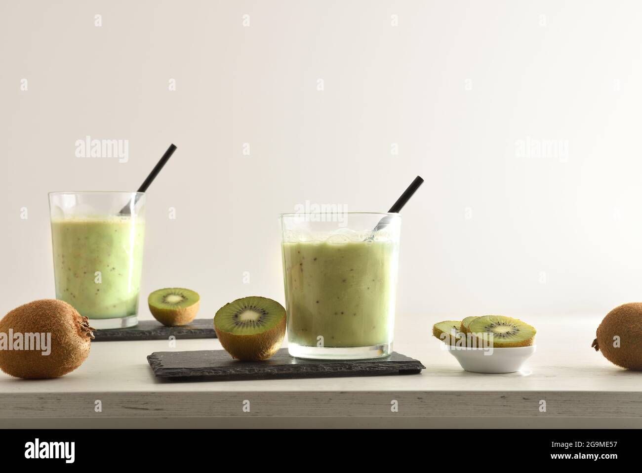 Zwei Gläser Kiwi-Getränk und Behälter mit geschnittenem Obst auf dem weißen Tisch. Vorderansicht. Stockfoto