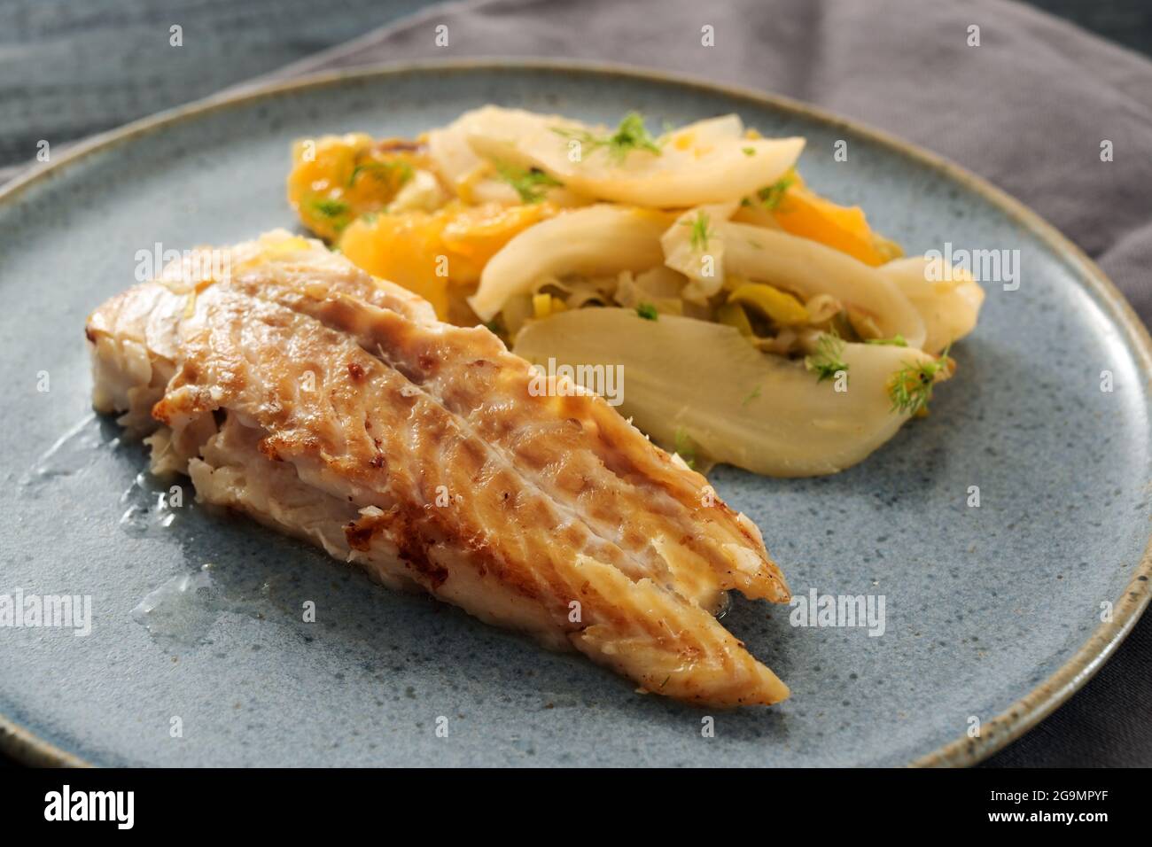 Sautierter Kabeljaufisch mit Fenchelgemüse und orangefarbenen Scheiben auf einem blauen Teller serviert, ausgewählter Fokus, enge Schärfentiefe Stockfoto