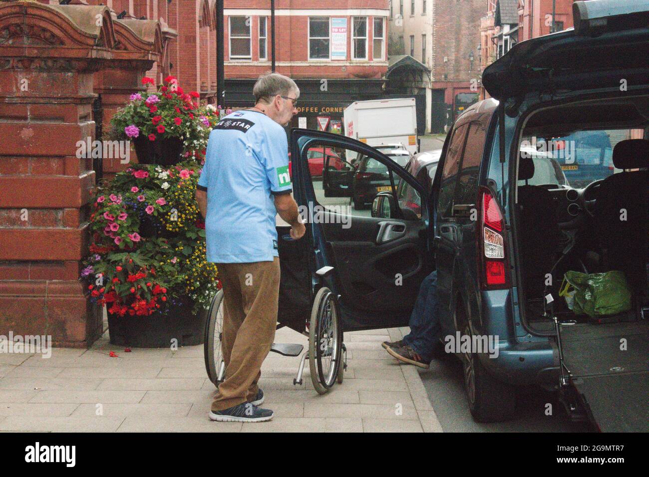 Mann, der einen Rollstuhl standfest hält, damit ein behinderter Passagier aus dem Auto aussteigen kann. Stockfoto