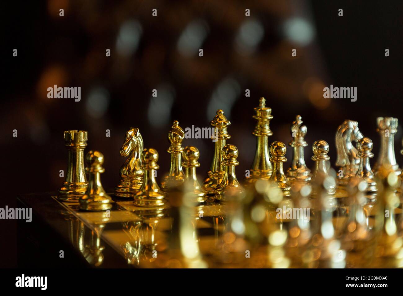 Nahaufnahme-Schachset mit vergoldeten Figuren und Ledersessel dahinter Stockfoto