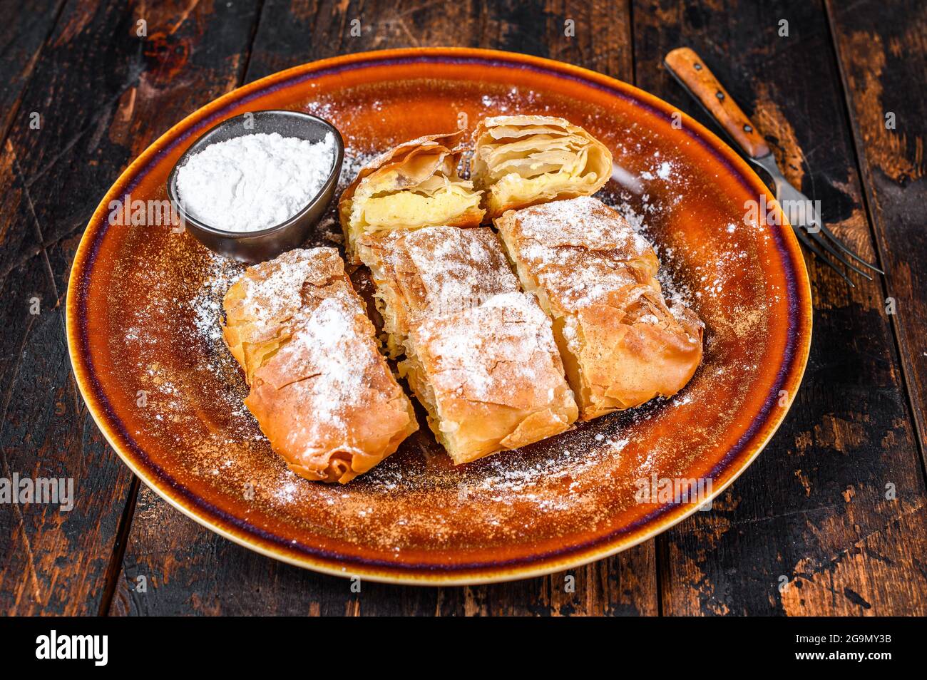 Griechischer Bougatsa-Kuchen in Scheiben mit Phyllo-Teig und Grießpudding-Sahne. Dunkler Holzhintergrund. Draufsicht Stockfoto