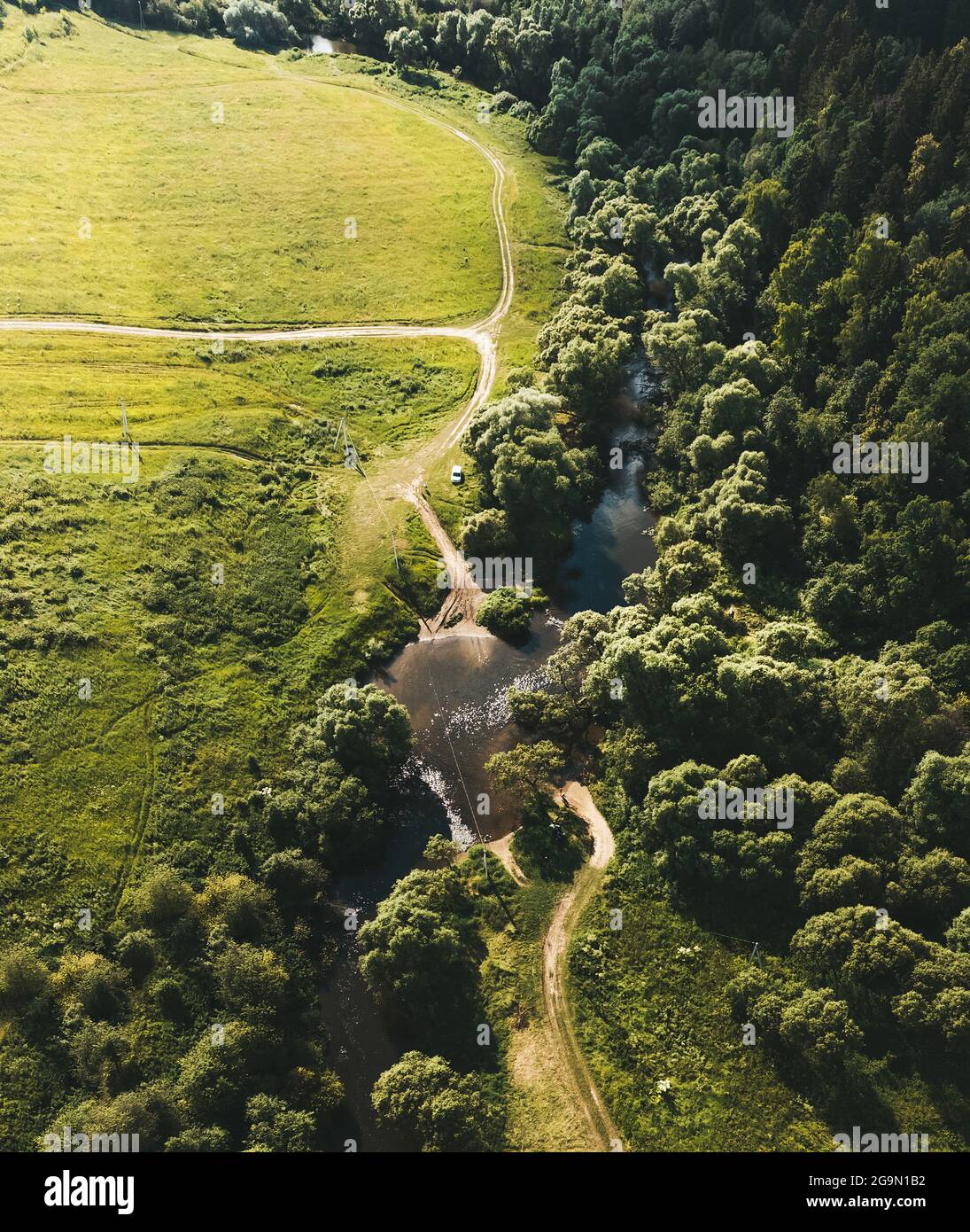 Kleiner Fluss zwischen dem Feld und dem Wald. Luftaufnahme. Vertikales Layout. Drohnenfotografie Stockfoto