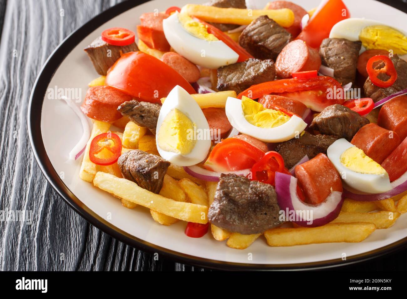 Pique Macho ist ein bolivianisches Gericht, das aus einer Schicht Pommes besteht, die unter einem Haufen gehacktes Rindfleisch, Würstchen, Eier, Tomaten, Zwiebeln, Paprika Stockfoto