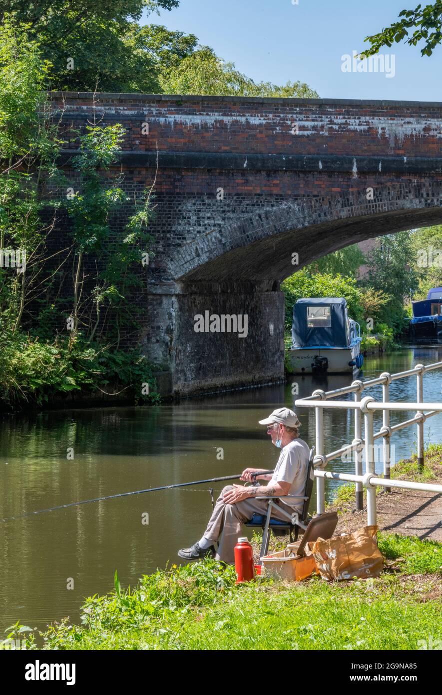 Mann sitzt in einem Stuhl Angeln an einem Sommertag auf dem Abfluss des bridgewater Kanal in manchester. Angler oder Fischer auf dem bridgewater Kanal. Stockfoto
