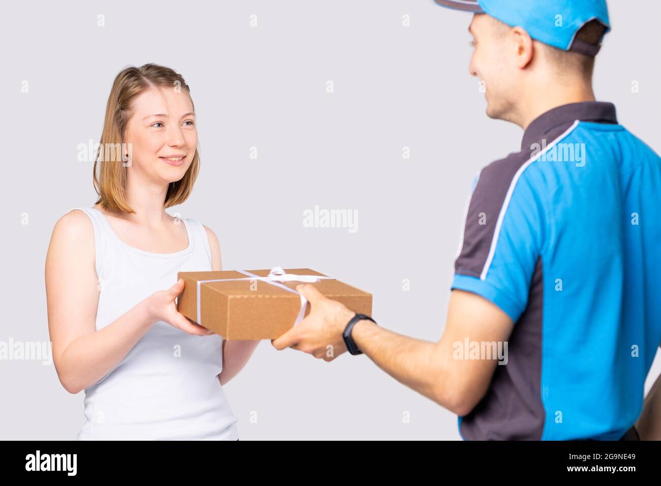 Zufriedene blonde Frau im weißen T-Shirt nimmt den Lieferkarton des Kuriermanns in Uniform. Stockfoto