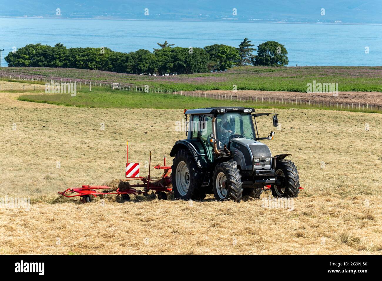 Traktor und Heubob drehen Heu in der Nähe von Portmahomack, Easter Ross, Schottland. Stockfoto