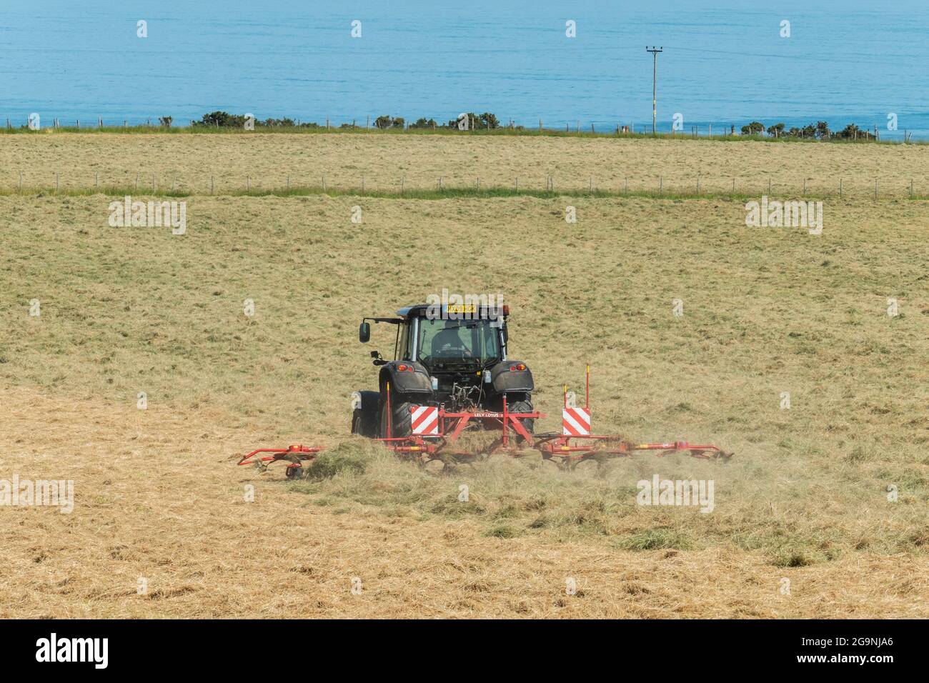 Traktor und Heubob drehen Heu in der Nähe von Portmahomack, Easter Ross, Schottland. Stockfoto