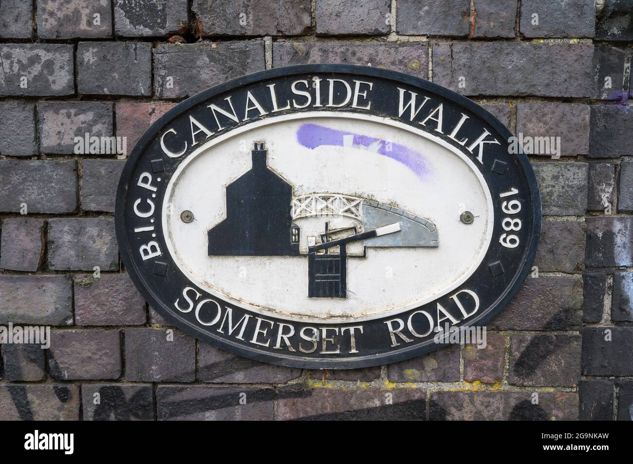 Ovale gusseiserne Plakette auf einer Backsteinmauer über dem Worcester und Birmingham Canal an der Somerset Road, die einen Spaziergang am Kanal in Birmingham, England, markiert. Stockfoto