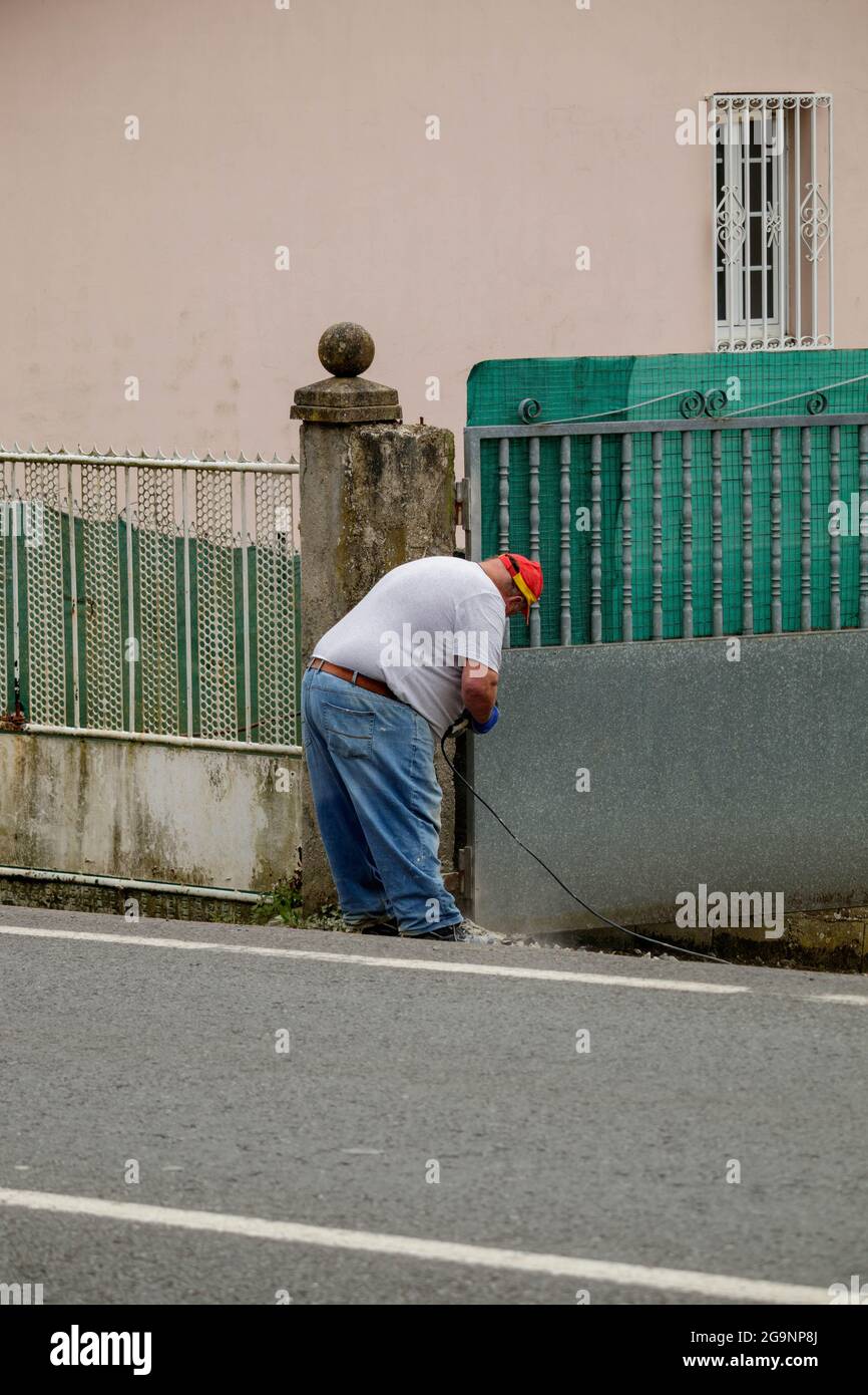 Coruna / Spanien - März 30 2021: Übergewichtiger Mann repariert eine Betonsäule mit einem Elektrowerkzeug in Spanien Stockfoto
