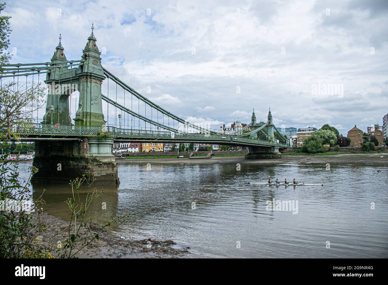 HAMMERSMITH LONDON 27 Juli 2021 . Ruderer passieren die Hammersmith Bridge in West London, die seit April 2019 für Kraftfahrzeuge und alle Nutzer im August 2020 für Radfahrer und Fußgänger wieder geöffnet ist. Hammersmith Bridge ist eine 253 m lange, 134 Jahre alte gusseiserne Hängebrücke, die letztes Jahr wegen Sicherheitskontrollen geschlossen wurde, nachdem Risse entdeckt wurden. Credit amer Ghazzal/Alamy Live News Stockfoto