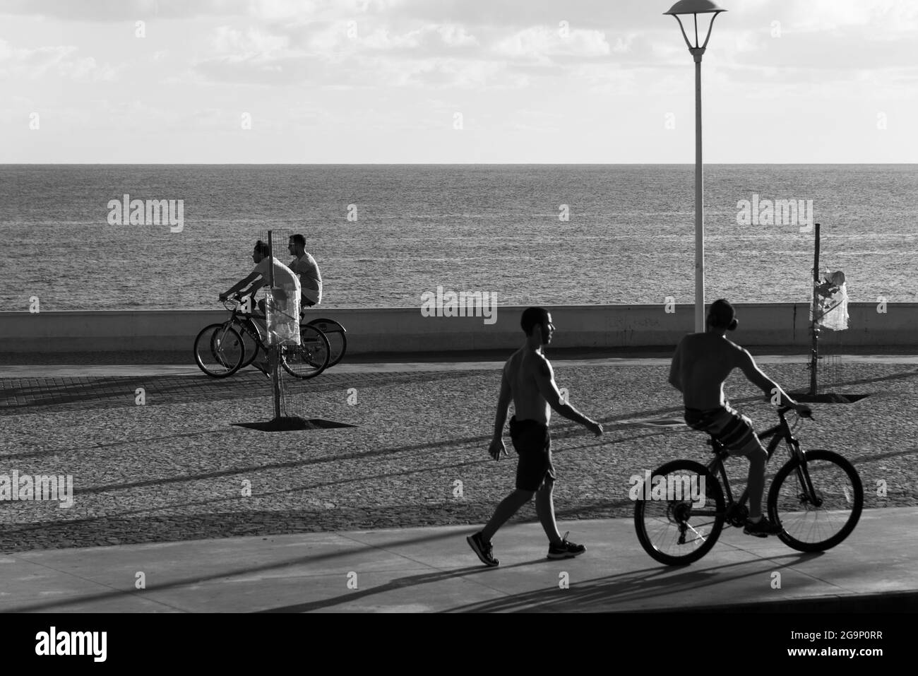 Salvador, Bahia, Brasilien - 16. Dezember 2018: Die Menschen fahren mit dem Fahrrad entlang der Strandpromenade von Rio Vermelho in Salvador. Ein Tag mit starkem Sonnenschein, der attra Stockfoto