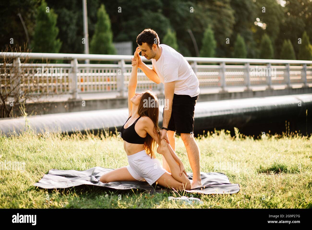 Personal Trainer Mann Coaching junge Frau, Yoga auf Stadtwiese, Sommerabend, fit Stockfoto
