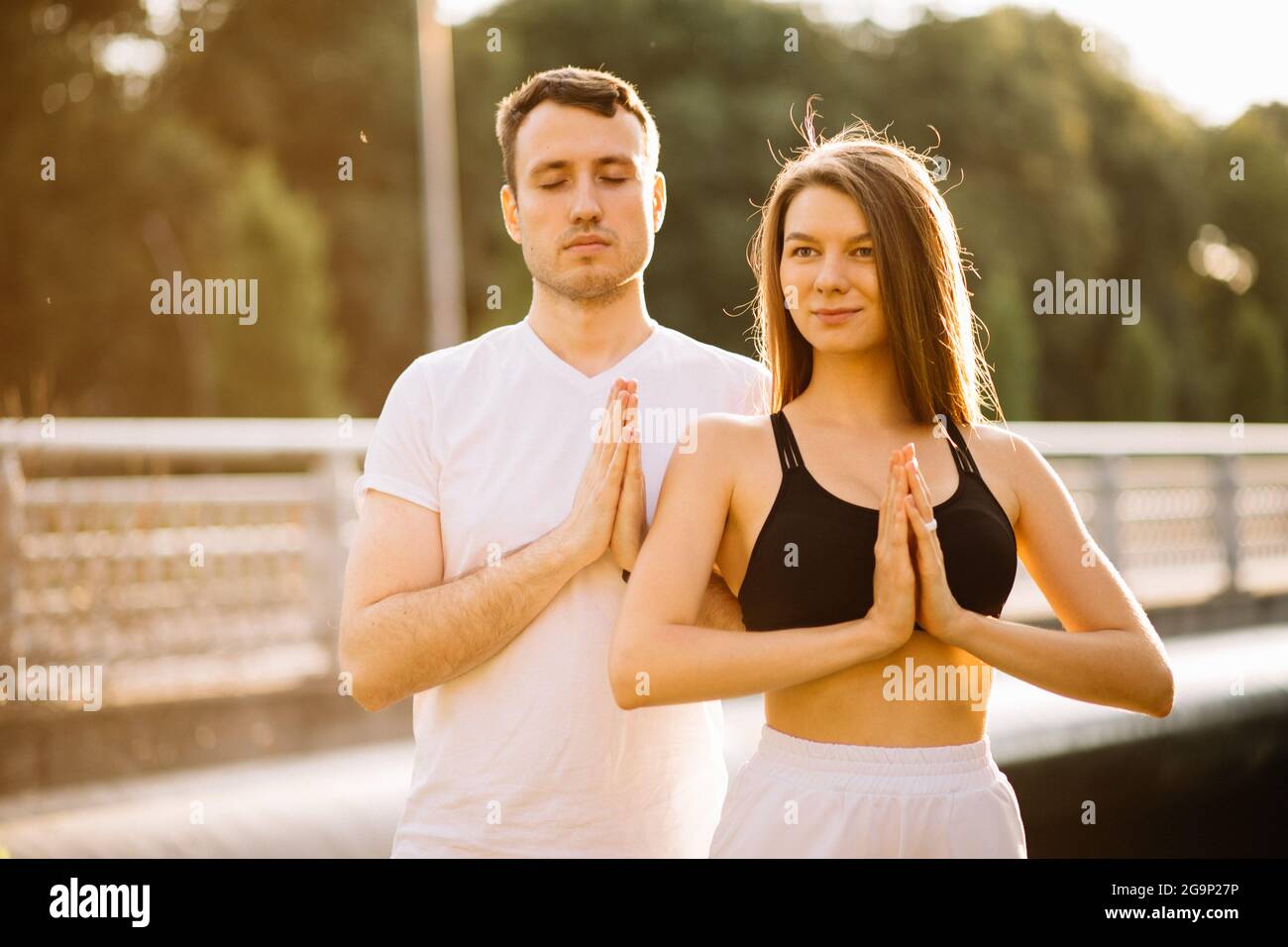 Junge Paar Mann und Frau meditieren zusammen, während sie stehen, Yoga auf dem Rasen der Stadt, Sommerabend, Lifestyle Stockfoto