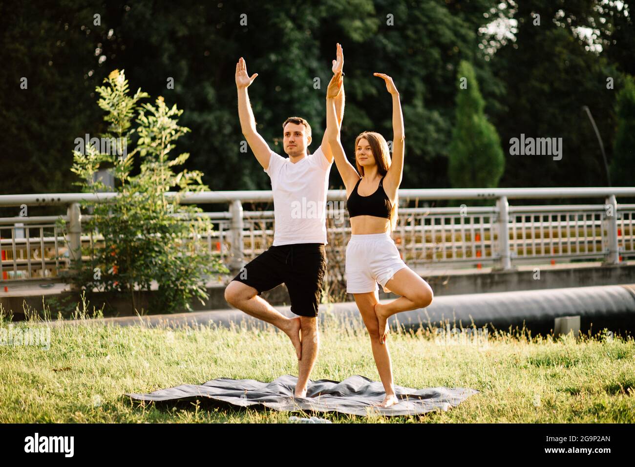 Junges Paar, Mann und Frau, die Sport treiben, Yoga auf dem Rasen der Stadt, Sommerabend, sich gemeinsam dehnen Stockfoto