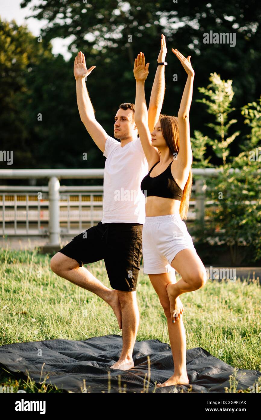 Junge Paar Mann und Frau, die Sport treiben, Yoga auf Stadtwiese, Sommerabend, Stretching Stockfoto