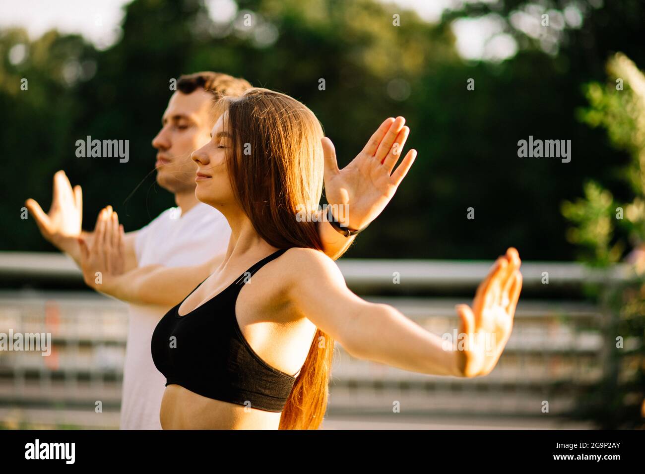 Das junge Paar, Mann und Frau, meditieren gemeinsam beim Sonnenuntergang, während sie stehen, Yoga auf dem Rasen, Sommerabend, Lebensstil, Atemübungen Stockfoto