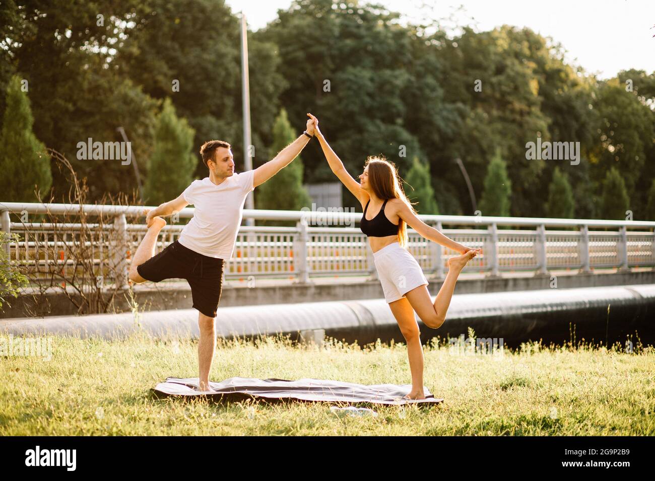 Junges Paar, Mann und Frau, die Sport treiben, Yoga auf dem Rasen der Stadt, Sommerabend, sich gemeinsam bei Sonnenuntergang ausstrecken Stockfoto