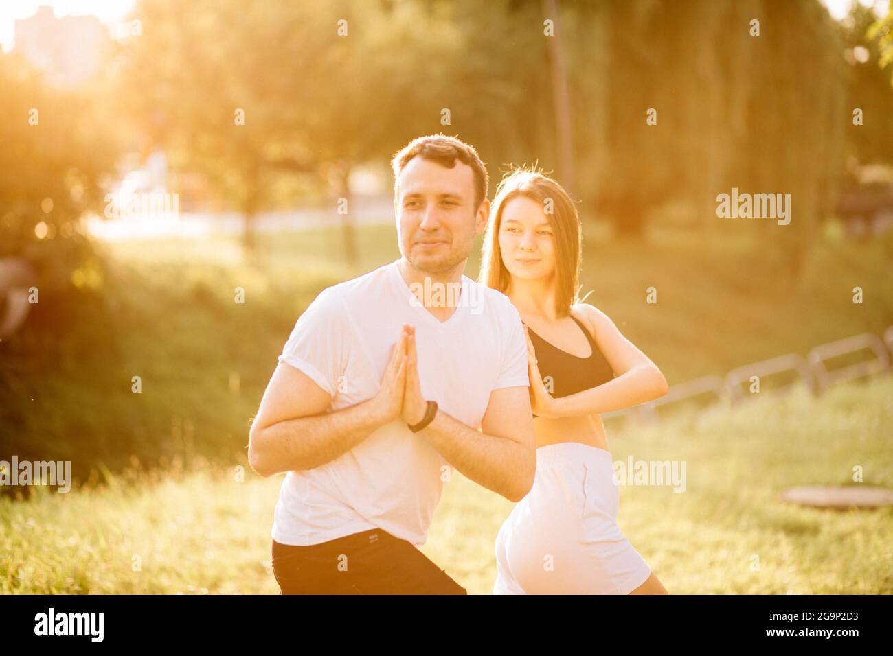 Junges Paar, Mann und Frau, die Sport treiben, Yoga auf dem Rasen der Stadt, Sommerabend, sich bei Sonnenuntergang gemeinsam dehnen, Konzentration Stockfoto