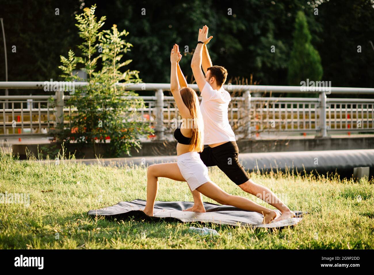 Junges Paar, Mann und Frau, die Sport treiben, Yoga auf dem Rasen der Stadt, Sommerabend, sich gemeinsam bei Sonnenuntergang ausstrecken, Lebensstil der Stadt Stockfoto