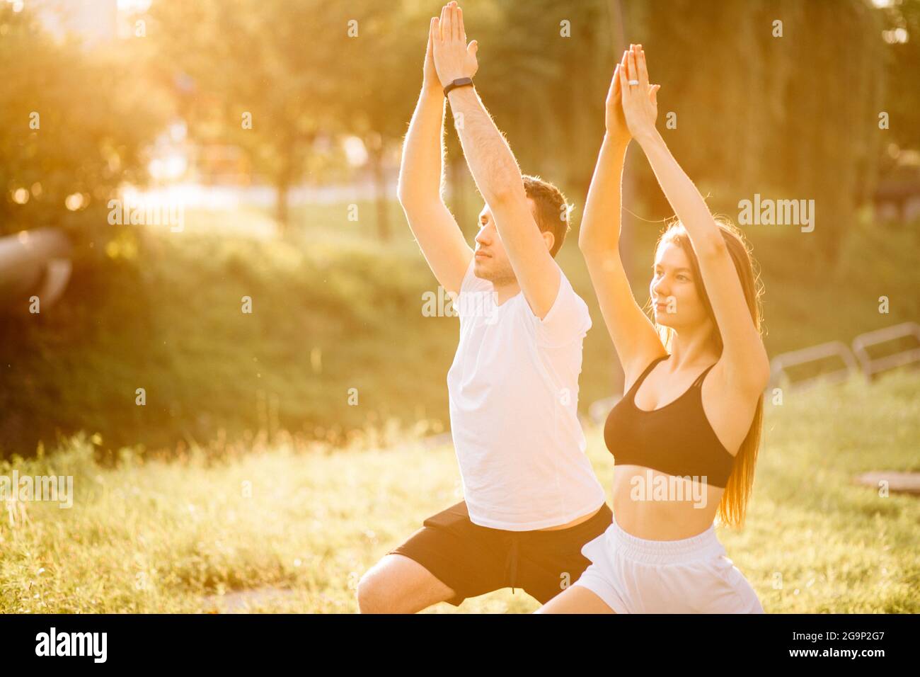 Körperteil Junges Paar von Mann und Frau, die Sport treiben, Yoga auf Stadtrasen, Sommerabend, Stretching zusammen am Sonnenuntergang, Stadtsport-Stil Stockfoto