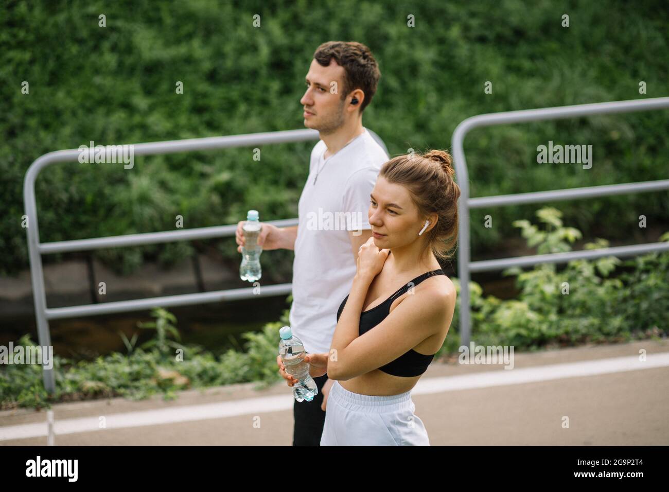 Junges glückliches Paar läuft im Stadtpark mit Wasserbotel in den Händen, gemeinsame Sportarten, Heiterkeit, Stadtsport gesunder Lebensstil, Fitness zusammen bei su Stockfoto