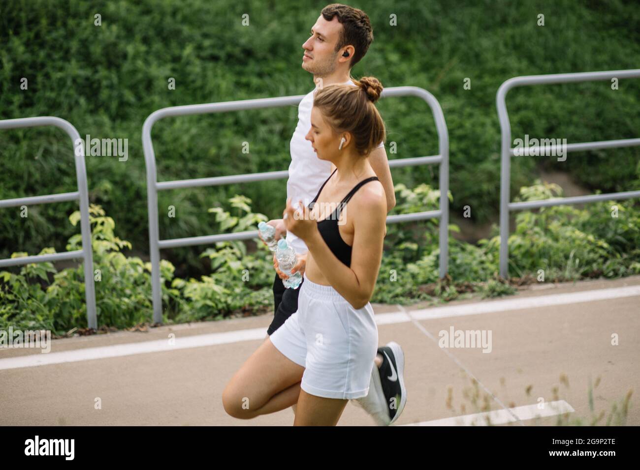 Junges glückliches Paar läuft im Stadtpark mit Wasserpfanne in den Händen, gemeinsame Sportarten, Heiterkeit, Stadtsport gesunder Lebensstil, Fitness zusammen bei ev Stockfoto