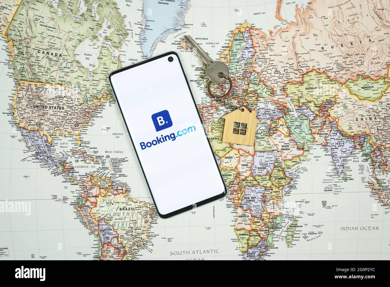 SWANSEA, Großbritannien - 4. JULI 2021: Smartphone mit Booking.com App-Logo mit Haus-Schlüsselanhänger und Schlüssel auf Weltkarte Hintergrund. App für die Buchung von Unterkünften Stockfoto