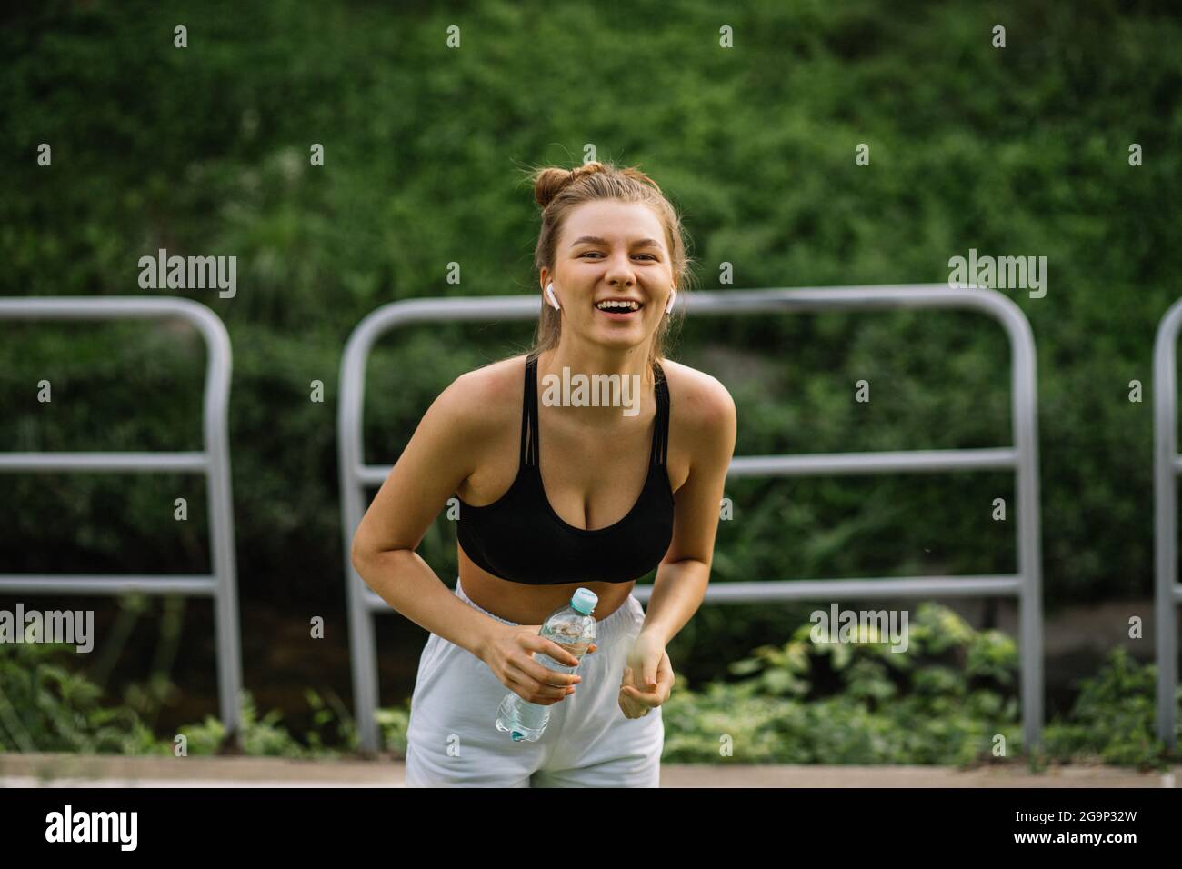 Junge schlanke nette glückliche Frau läuft im Stadtpark mit Wasserpfanne in den Händen, Sport, Heiterkeit, Stadtsport gesunder Lebensstil, Fitness, lachende ru Stockfoto