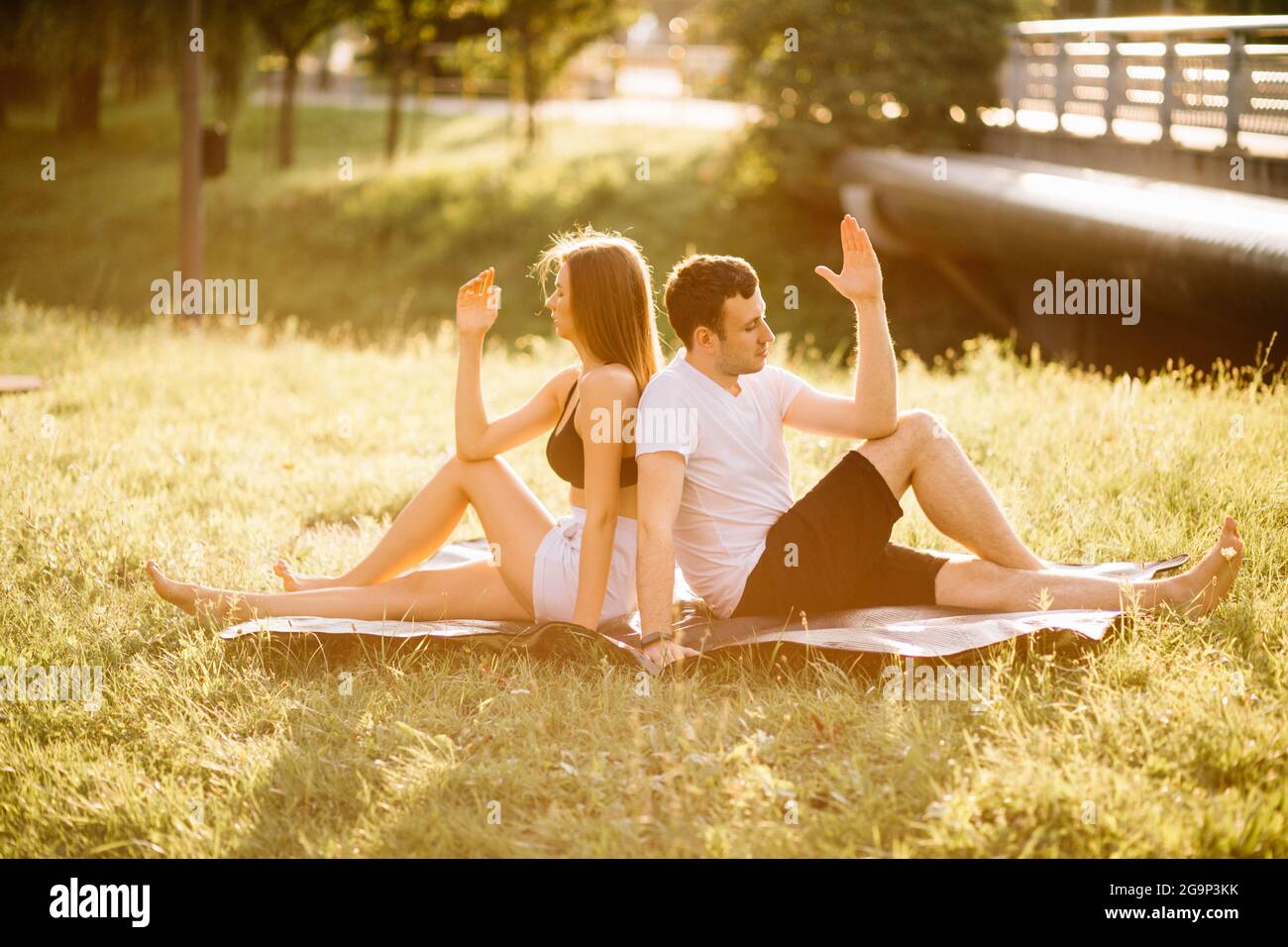 Junges Paar, Mann und Frau, die Sport treiben, Yoga auf dem Rasen der Stadt, Sommerabend zusammen Stockfoto