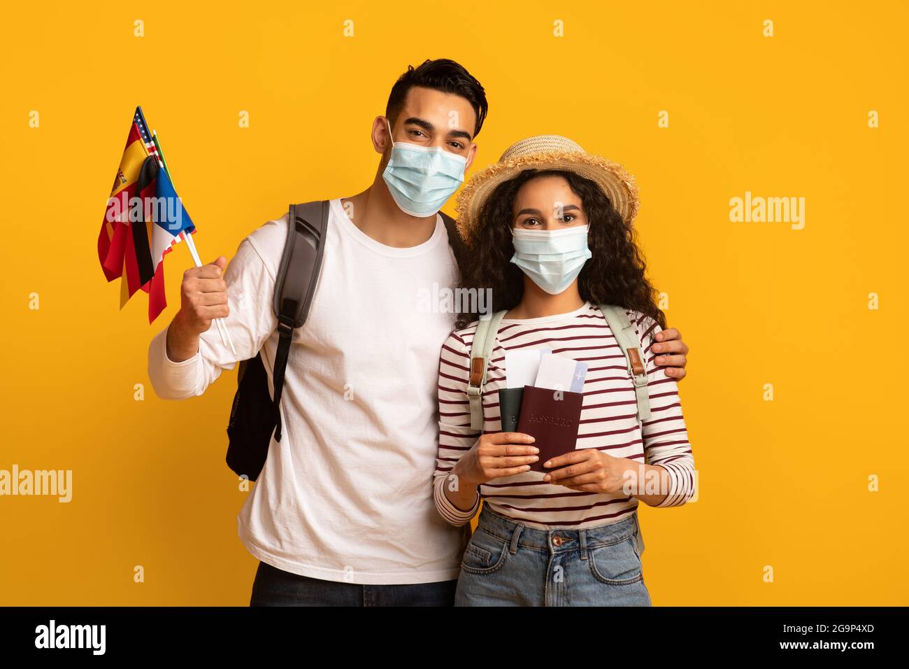 Pandemie Reist. Junges Paar Mit Medizinischen Masken, Die Pässe Und Internationale Flaggen Tragen Stockfoto