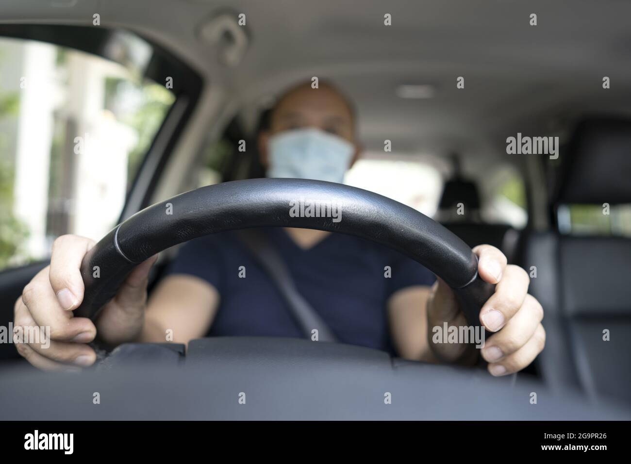 Shallow-Focus-Aufnahme eines südostasiatischen Mannes in einer Maske, die ein Auto fährt Stockfoto